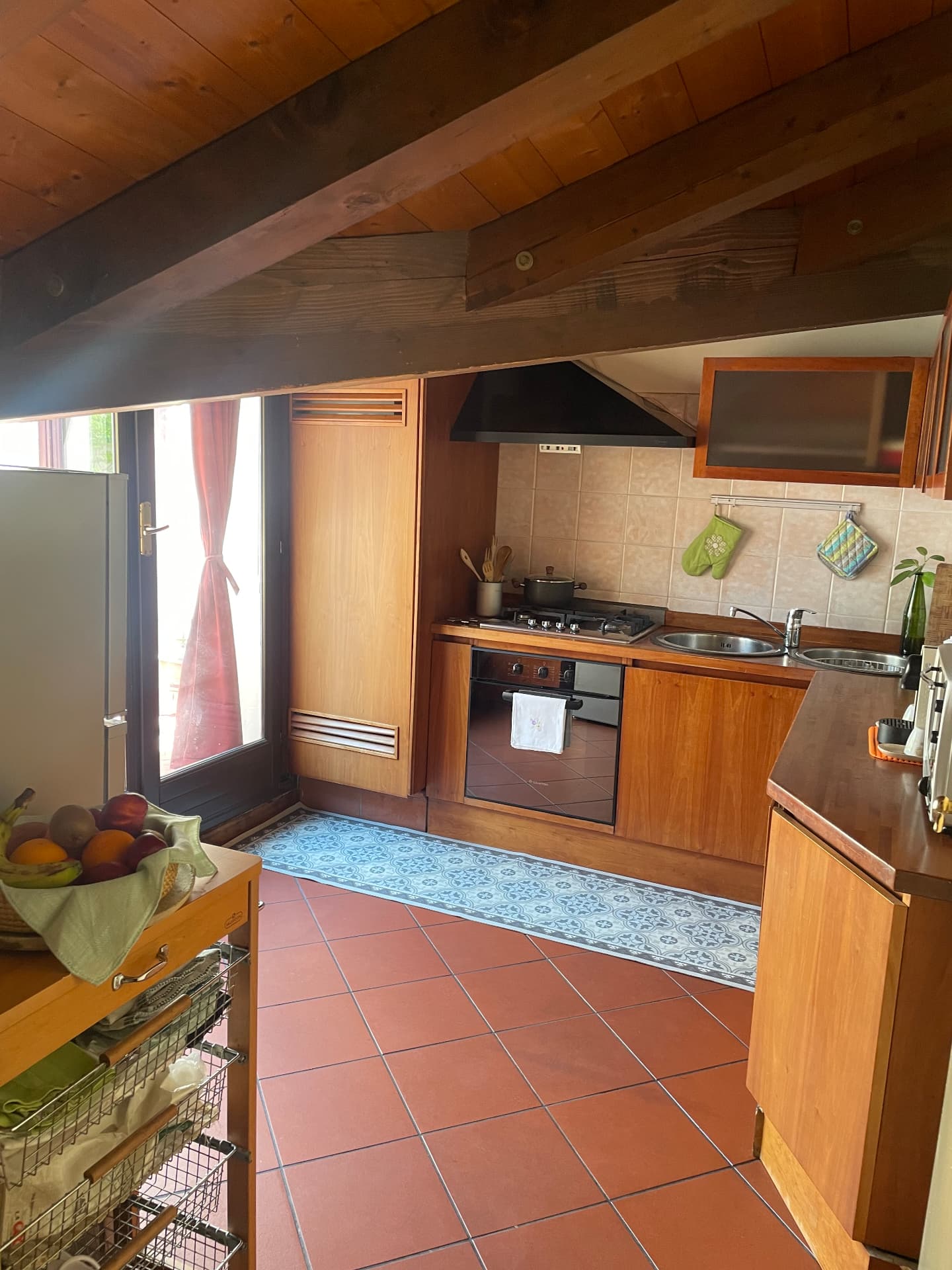 Kitchen with beamed ceiling, gas hob, oven, fridge and a door opening to daylight