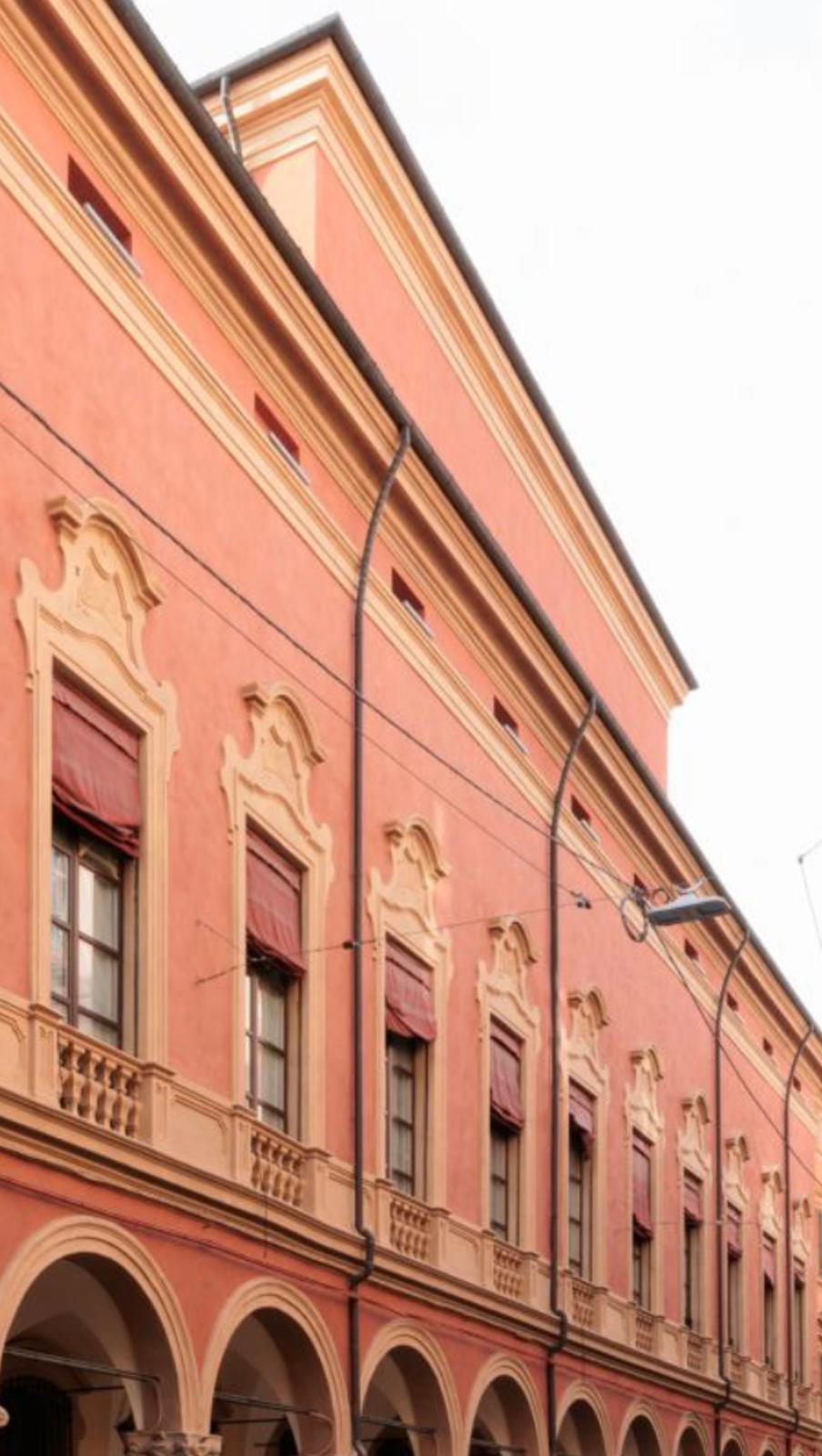 Terracotta facade of the historic palazzo with arched portico, ornate window frames and red awnings