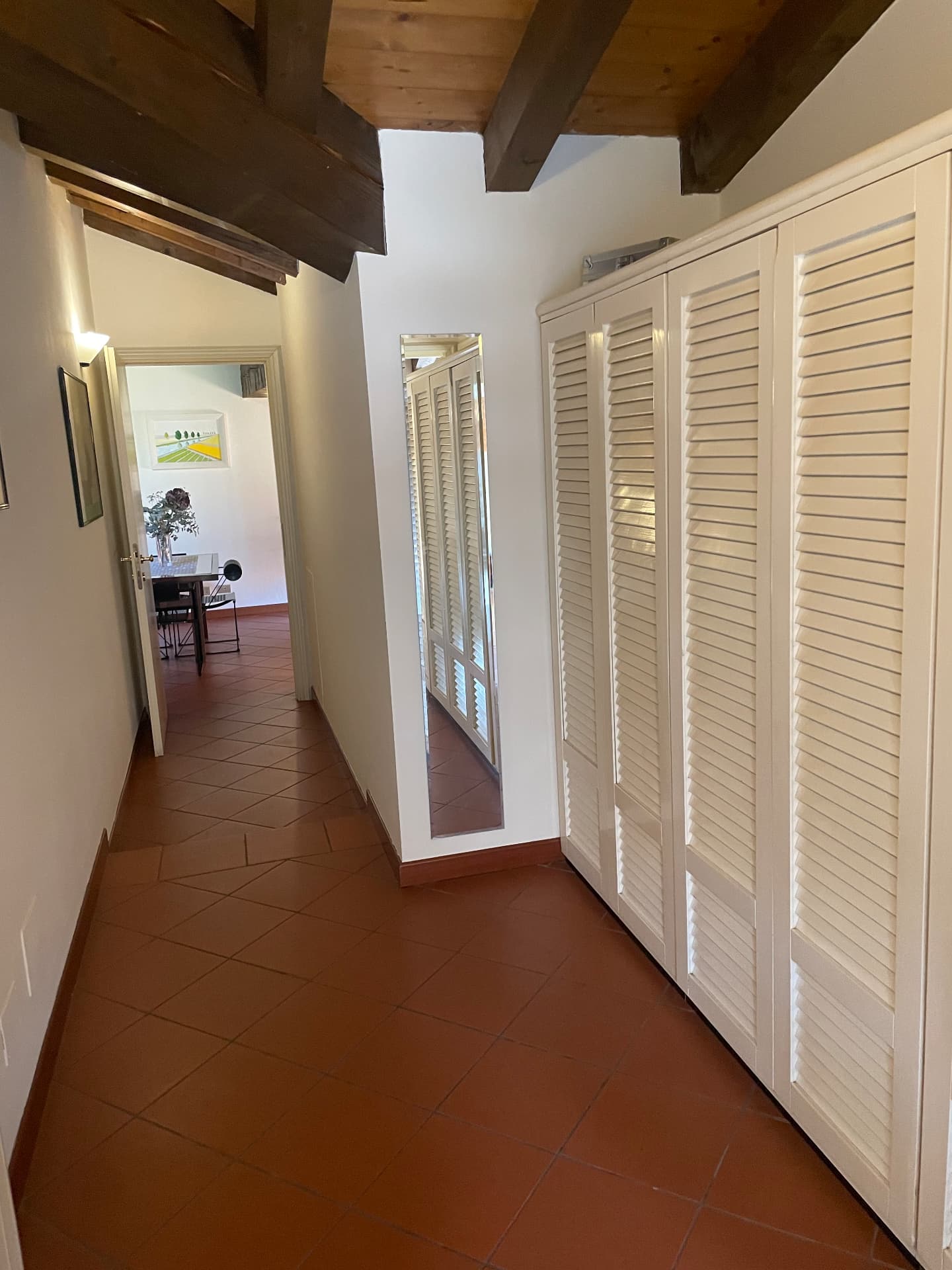 Corridor with terracotta floor tiles, louvred wardrobe doors, a full-length mirror and beamed ceiling