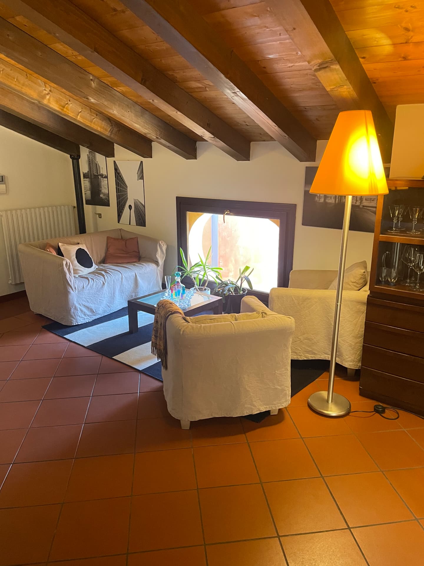 Living room with sofa, armchairs, floor lamp and a square window under wooden beams